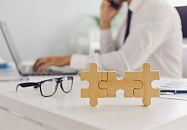 3 Puzzleteile ineinander gesteckt liegen auf einem Schreibtisch, davor eine Brille