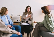 Drei Personen sitzen auf Sesseln und Sofa und beraten sich