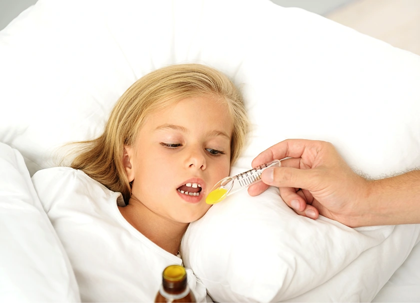 Kind liegt auf einem weißen Kissen und erhält von einem Löffel einen gelben Saft.