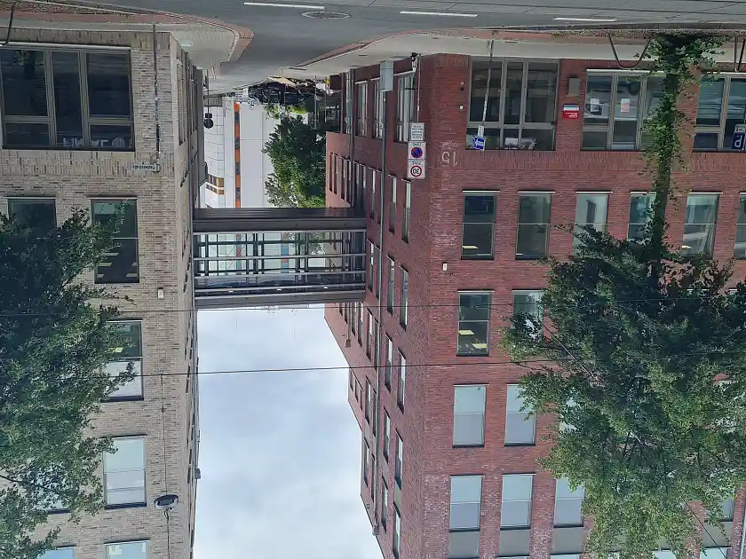 Das Dienstgebäude von außen vor der Nachrüstung. Man sieht eine Glasbrücke, die zwei Gebäude verbindet.