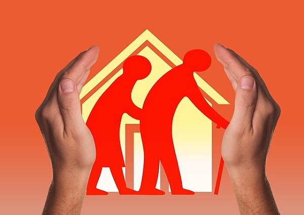 Zwei Hände halten ein Haus vor dem zwei ältere Menschen mit Krücke abgebildet sind.