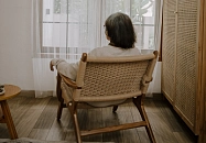 Frau sitzt im Schaukelstuhl vor einem Fenster